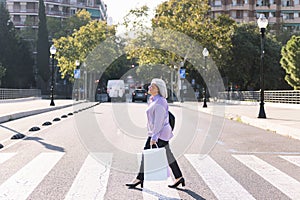 senior woman crossing a street with shopping bags