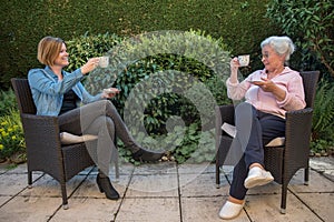 Senior woman and daughter having coffee at safety distance in the garden,