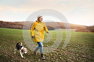 Senior woman with dog on a walk in an autumn nature.