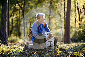 A senior woman with dog on a walk outdoors in forest, resting.