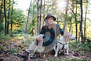 A senior woman with dog on a walk outdoors in forest, resting.