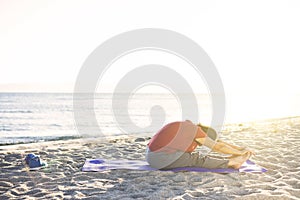Senior woman doing exercise on yoga mat at the beach, back stretching