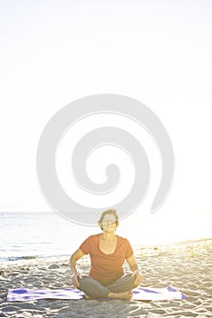 Senior woman doing exercise on yoga mat at the beach, eyes closed