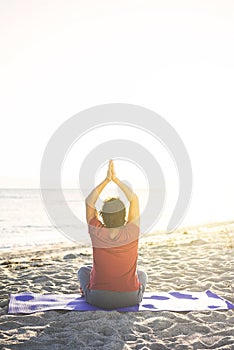 Senior woman doing exercise on yoga mat at the beach, meditating. Shot from back