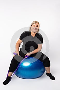 Senior woman doing exercises on a fitness ball and with an elastic band. Photo on a white background