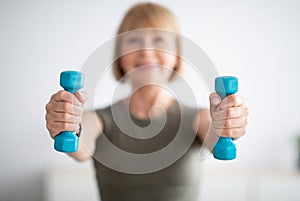 Senior woman doing fitness exercises with weights at home, focus on hands holding dumbbells