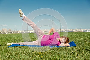 Senior woman doing sport training on the green grass in public park.