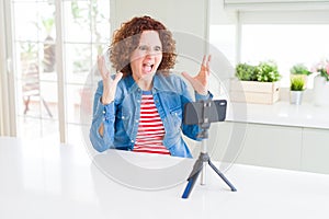 Senior woman doing video chat using smartphone camera crazy and mad shouting and yelling with aggressive expression and arms