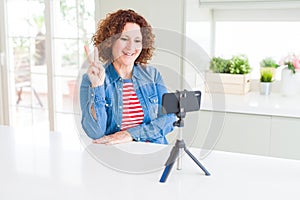 Senior woman doing video chat using smartphone camera smiling with happy face winking at the camera doing victory sign