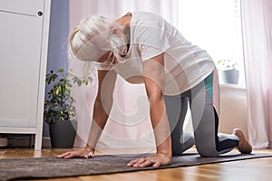 Senior woman doing yoga exercise in the room downward facing cat pose