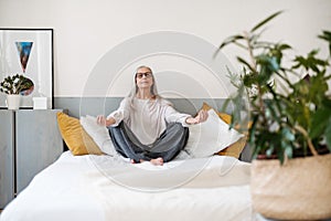 Senior woman doing yoga and meditating on her bed.