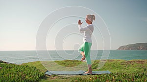 Senior woman doing yoga on ocean shore in tree pose