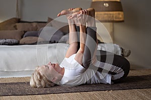 Senior woman doing yoga in sunny room. Happy Baby Pose