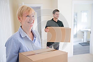 Senior Woman Downsizing In Retirement Carrying Boxes Into New Home On Moving Day With Removal Man Helping