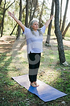 Senior woman with dreadlocks in stretching position on nature at morning. Elderly woman doing yoga on park - wellbeing