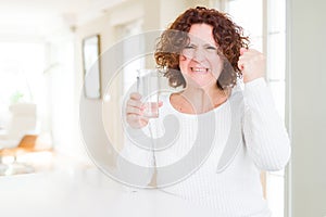 Senior woman driking a fresh glass of water annoyed and frustrated shouting with anger, crazy and yelling with raised hand, anger