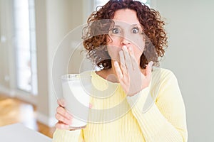 Senior woman drinking a glass of fresh milk cover mouth with hand shocked with shame for mistake, expression of fear, scared in