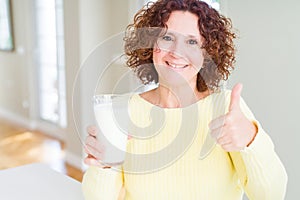 Senior woman drinking a glass of fresh milk happy with big smile doing ok sign, thumb up with fingers, excellent sign