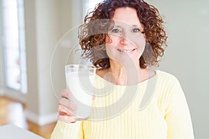 Senior woman drinking a glass of fresh milk with a happy face standing and smiling with a confident smile showing teeth