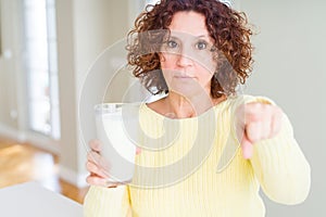 Senior woman drinking a glass of fresh milk pointing with finger to the camera and to you, hand sign, positive and confident