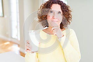 Senior woman drinking a glass of fresh milk serious face thinking about question, very confused idea