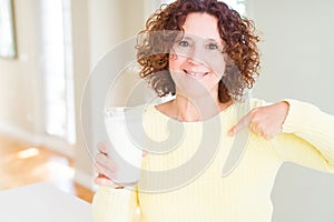 Senior woman drinking a glass of fresh milk with surprise face pointing finger to himself
