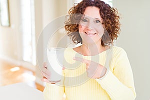 Senior woman drinking a glass of fresh milk very happy pointing with hand and finger