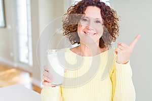 Senior woman drinking a glass of fresh milk very happy pointing with hand and finger to the side