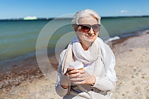 Senior woman drinking takeaway coffee on beach