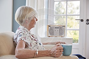 Senior woman drinking tea and listening to radio at home