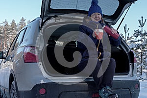 Senior woman drinking tea while sitting in back of suv after wintry forest trail. Outdoor activities to boost mood during