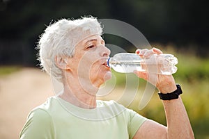 Senior woman drinking water after exercising, summer time, portrait in the park