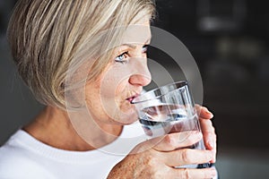 Senior woman drinking water in the kitchen.