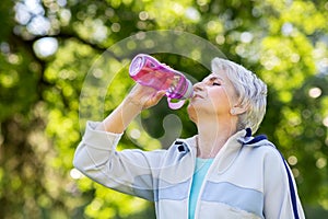 Senior woman drinks water after exercising in park