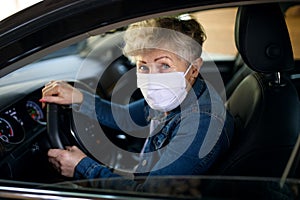Senior woman driver with face mask in car, quarantine concept.