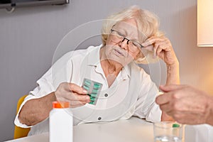 senior woman with drugs in hands reading prescription of medication, sitting alone at home