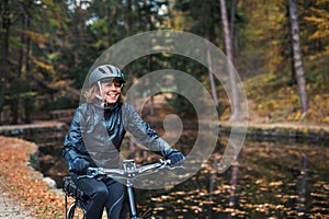 A senior woman with electrobike cycling outdoors on a road in park in autumn.