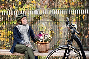 A senior woman with electrobike and flowers sitting on a bench outdoors in town.