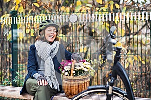 A senior woman with electrobike and flowers sitting on a bench outdoors in town.