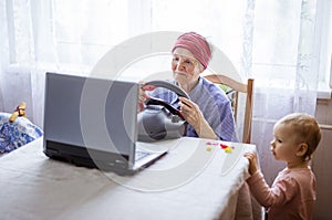 Senior woman enjoying car racing video game on laptop while her great granddaughter watching her play
