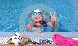 Senior woman enjoying swimm into the outdoors pool with swimming goggles and cap - active elderly female enjoying healthy activity