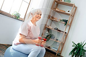 Senior woman exercise at home sitting on exercise ball holding dumbbells