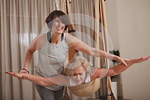 Senior woman exercising at with fly yoga trainer