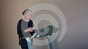 Senior Woman Exercising On Treadmill At Home Wearing Wireless Earphones