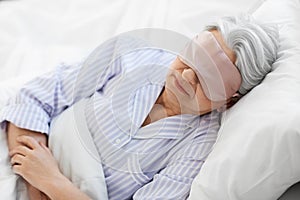 senior woman with eye mask sleeping in bed at home