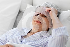 senior woman with eye sleeping mask in bed at home
