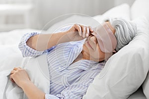senior woman with eye sleeping mask in bed at home