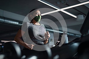 Senior woman with face mask doing exercise on treadmill in gym, coronavirus concept.