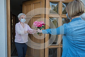 Senior woman with face mask gets flowers at the house door from neighbor woman