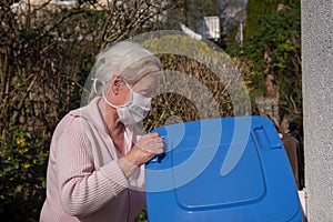 Senior woman with face mask opening garbage can